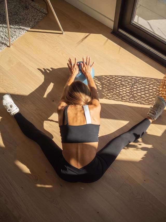 Person stretching on a wooden floor with sunlight casting shadows