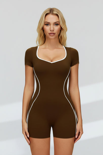 A woman modeling a brown short-sleeve bodysuit with white contrast trim along the scoop neckline, armholes, and side seams, photographed against a light gray studio background.