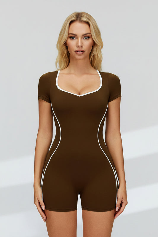 A woman modeling a brown short-sleeve bodysuit with white contrast trim along the scoop neckline, armholes, and side seams, photographed against a light gray studio background.