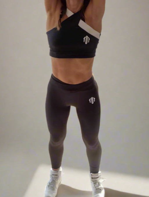 Woman in workout attire stretching in a room with plants and large windows.